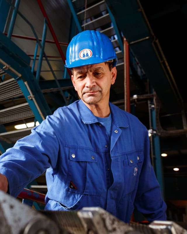 Technicien en bleu de travail et casque réglant une machine dans un atelier de production